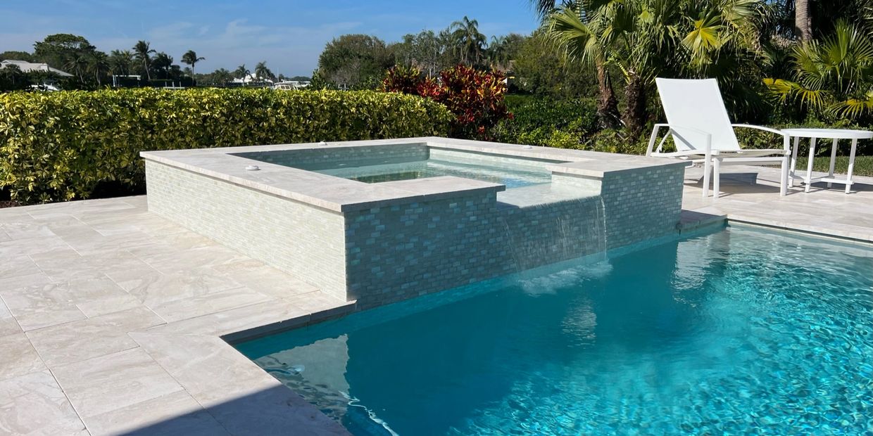 Modern pool with an elevated spa and cascading water feature in a lush backyard.