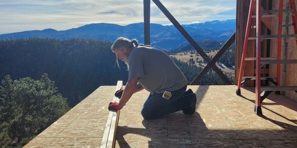 Man working on wooden construction with mountain backdrop under bright sun overlooking Northern Colorado Loveland Ft Collins Greeley Mead Milliken Evans
