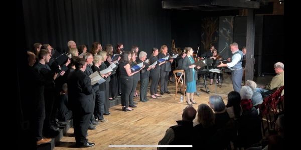 Choir performing on stage with conductor and audience watching.