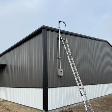 Ladder leaning against a metal building with tools on the ground.