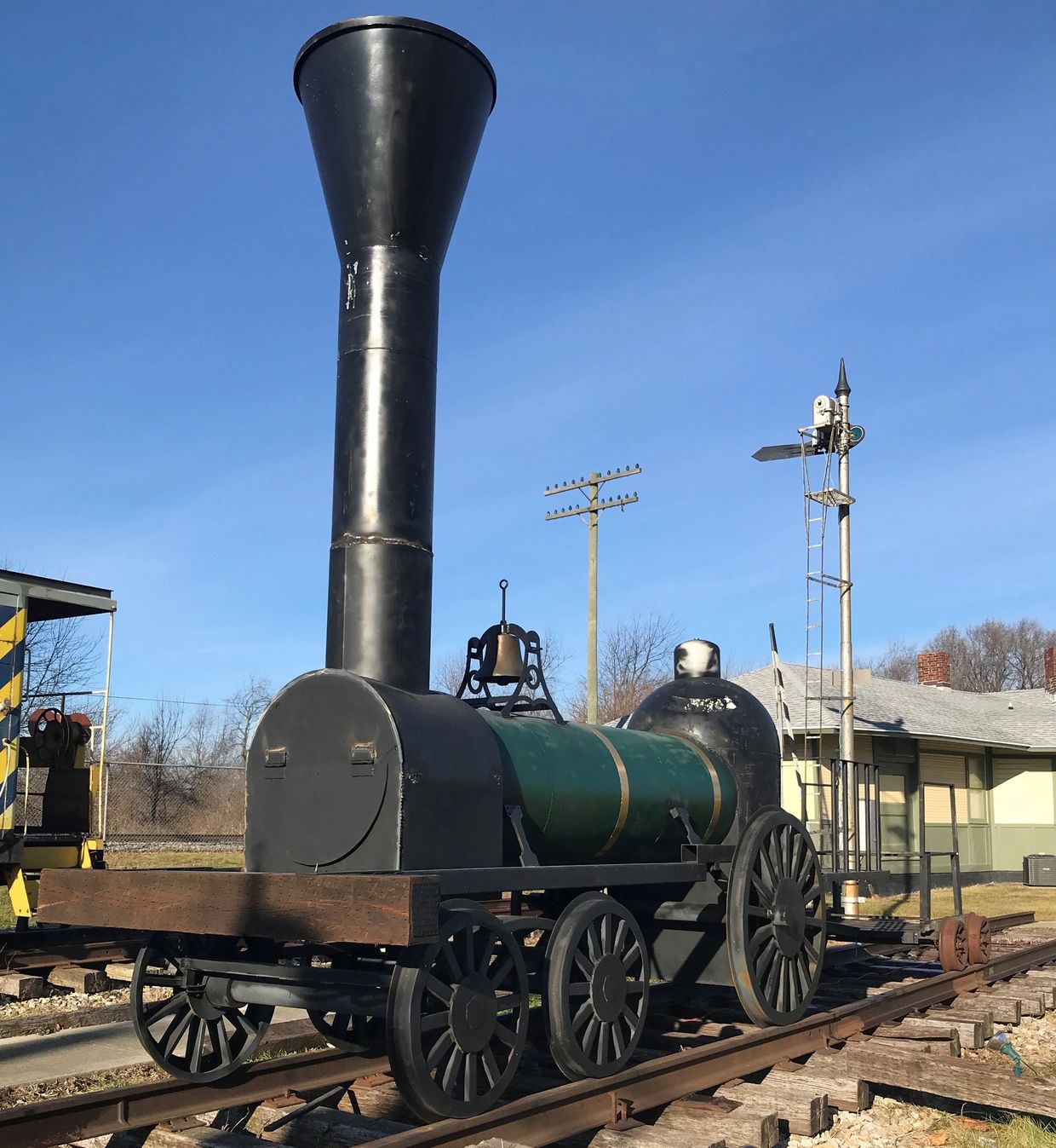 A vintage black and green steam locomotive on railroad tracks under clear blue sky.
