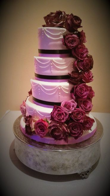 Elegant four-tiered white cake with dark red roses and black bands.
