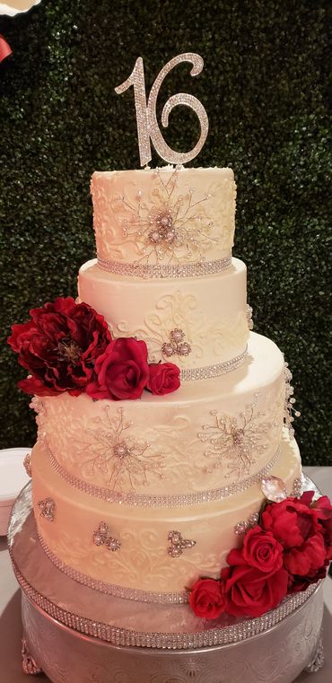 Elegant four-tier white cake with red flowers and a silver '16' topper.