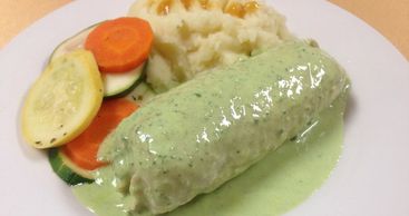 Dish with mashed potatoes, steamed vegetables, and creamy green sauce.