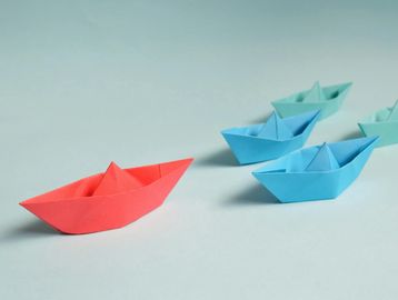 Red paper boat leading two blue and two teal paper boats.