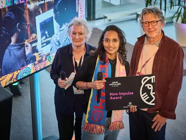Three people holding New Impulse Award sign and microphones indoors.