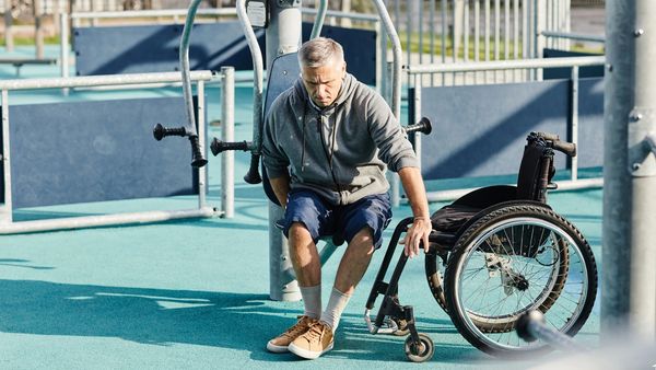 a disabled man climbing onto a wheelchair after using a disabled friendly outdoor gym machine