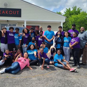 A diverse group of young people and adults posing outside a building with a 'BREAKOUT' sign.