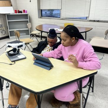 Two girls using a tablet at a classroom table.