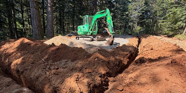 Green excavator digging a trench in a forest.