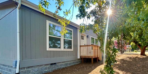 Sunlit house exterior with wooden porch and surrounding trees.