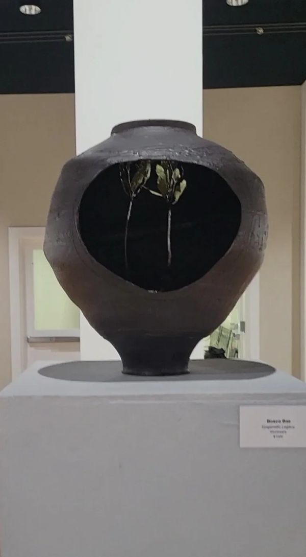 Dark round ceramic vase with a hollow center and two small dried plants inside.
