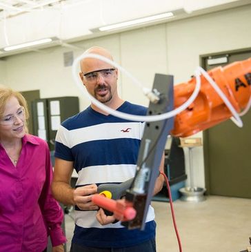 Two people observing an industrial robot arm at work.
