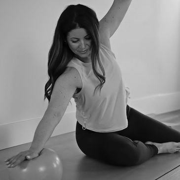 Woman practicing yoga with an exercise ball on a mat indoors.