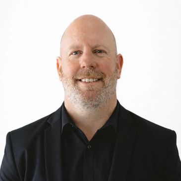 Smiling bald man in a black suit against a white background.