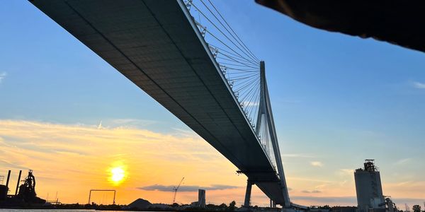 A cable-stayed bridge at sunset over water with industrial buildings nearby.