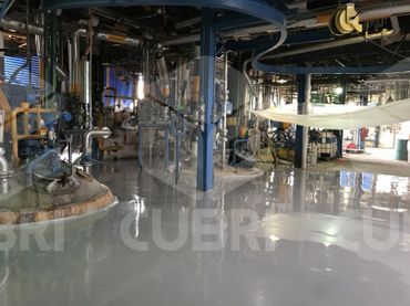 Industrial plant interior with machinery and a shiny, reflective floor coating.