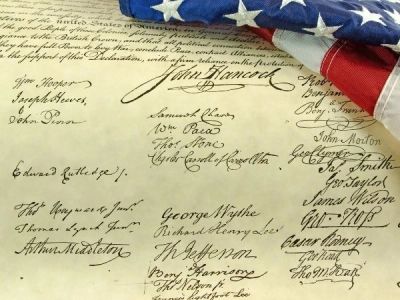 American flag draped over historic document with signatures.