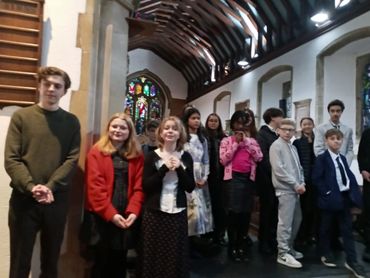 Group of young people standing inside a church with stained glass windows.