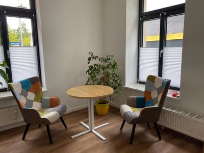 Cozy corner with two patchwork armchairs, round wooden table, and a potted plant by windows.