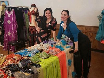 Two women smiling behind a table displaying colorful fabrics and garments.