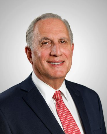 Professional headshot of an older man in a suit and red tie.