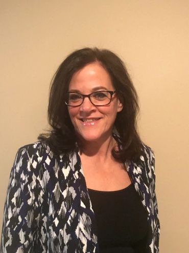 Smiling woman with glasses and patterned jacket.