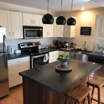 Modern kitchen with white cabinets, black countertops, stainless steel appliances, and a central island with stools.