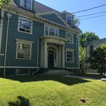 Blue house with columns and a well-maintained lawn on a sunny day.