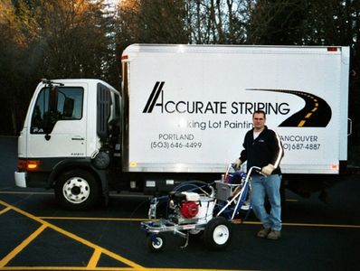 Man standing next to a parking lot striping machine in front of a truck with 'Accurate Striping