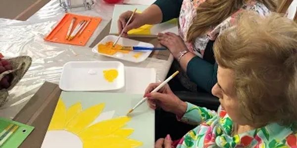 Two women painting a sunflower on canvas.