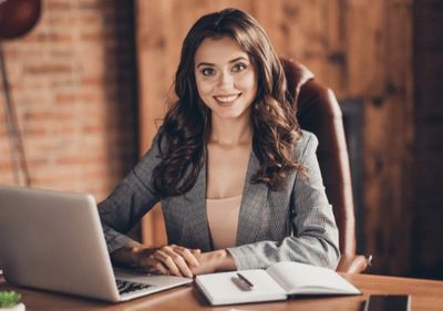 Young woman in business attire smiling at her desk.