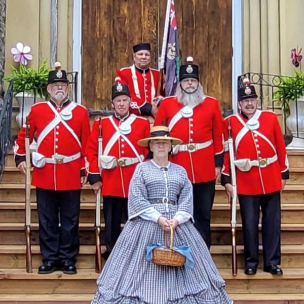 Group in Victorian-era military and civilian attire posing on steps.