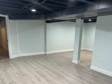 Empty finished basement with light wood flooring and pillar.