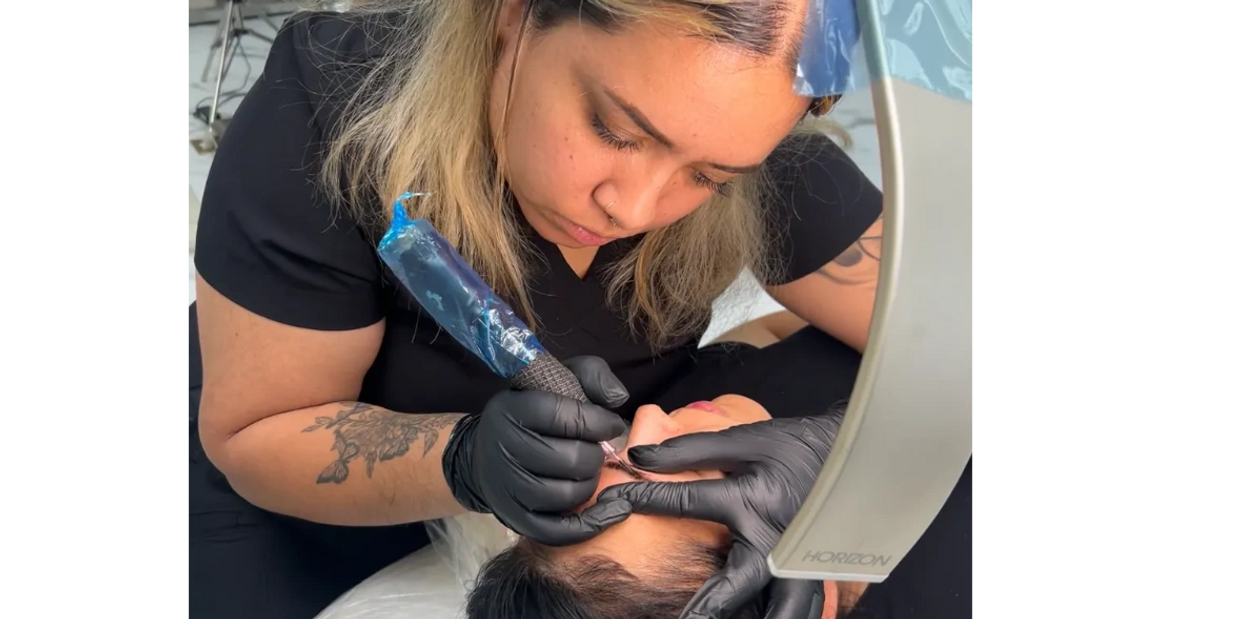 A tattoo artist intensely working on a client's eyebrow tattoo.