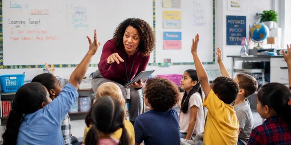 Teacher engaging young students raising hands in classroom discussion.