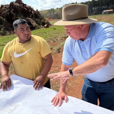 Two men discussing a blueprint outdoors on a sunny day.