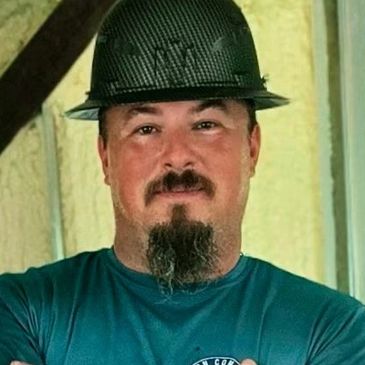 Man in a construction site wearing a hard hat and teal shirt.