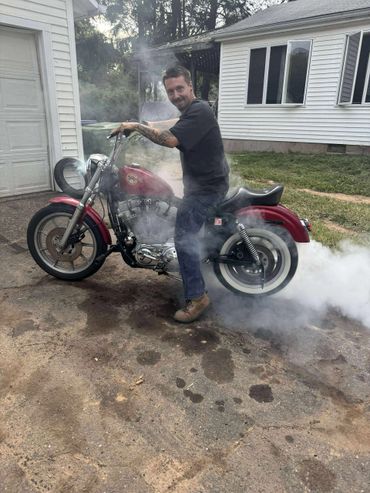 Man performing a burnout on a red motorcycle in a driveway.