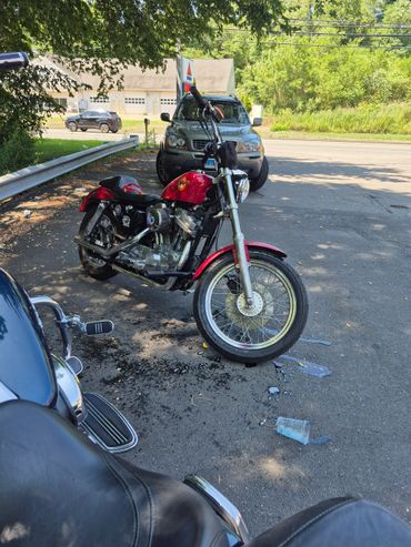 A red motorcycle parked on asphalt near a car and roadside.