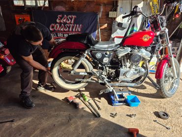Man inspecting a red Harley-Davidson motorcycle in a garage with tools scattered on the floor.