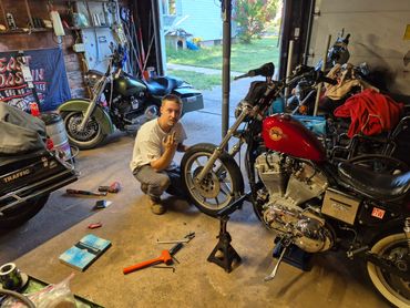 Man working on a motorcycle in a cluttered garage.