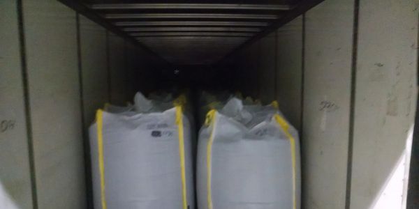 Large white bulk bags with yellow edges stored inside a container or truck.