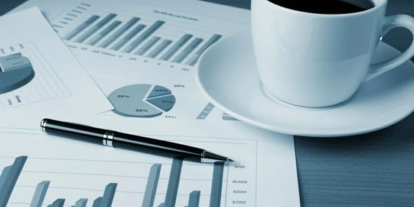 A cup of coffee beside charts and a pen on a desk.