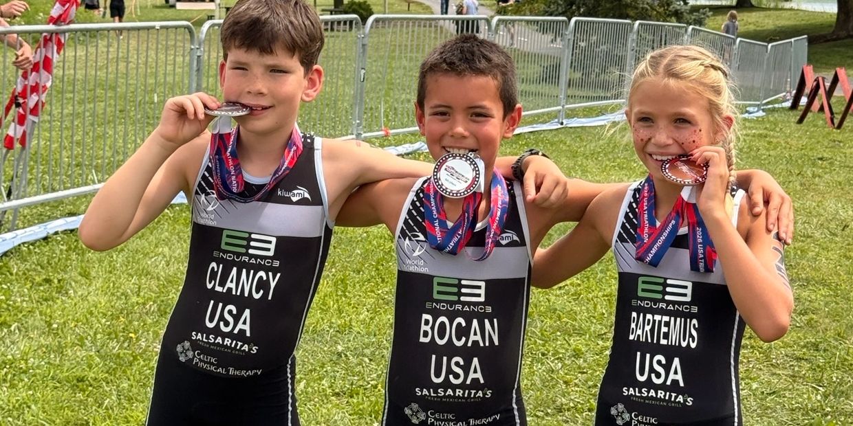 Three kids celebrate with medals at a triathlon.