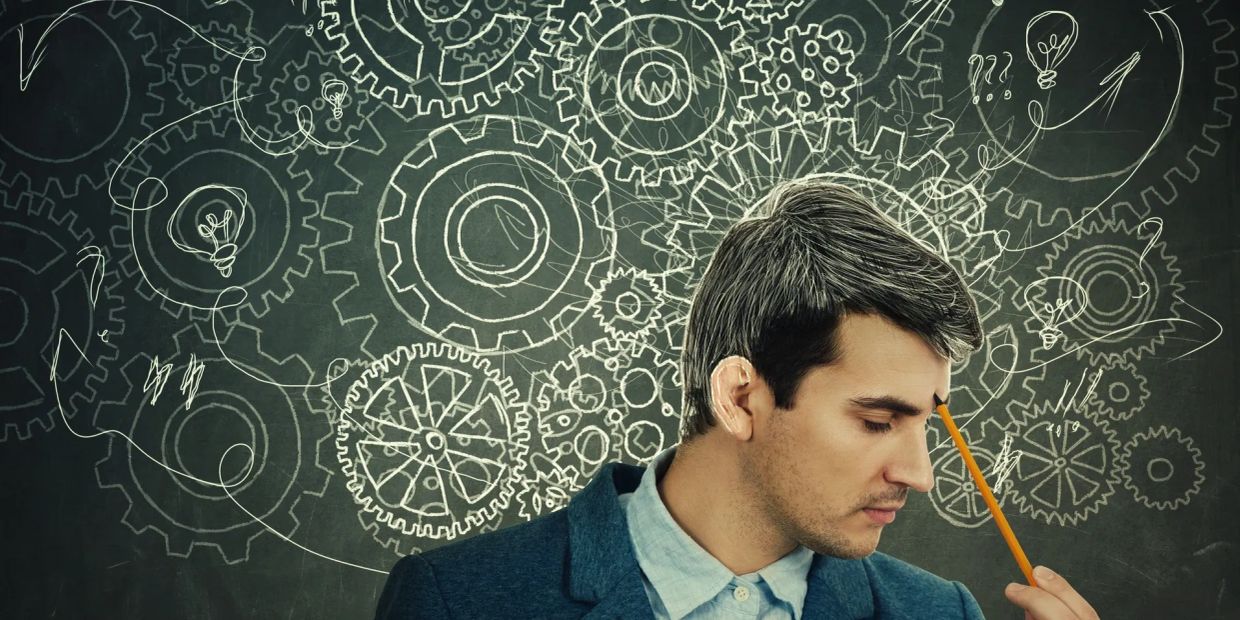 Man deep in thought with gears and light bulbs on chalkboard.