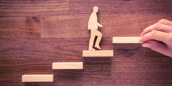 Wooden figure climbing wooden stairs symbolizing progress.