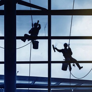 Silhouetted window washers suspended outside a large glass building.