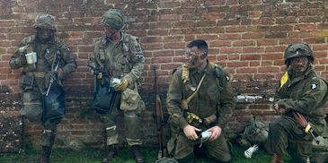 Four soldiers in military gear resting against a brick wall.