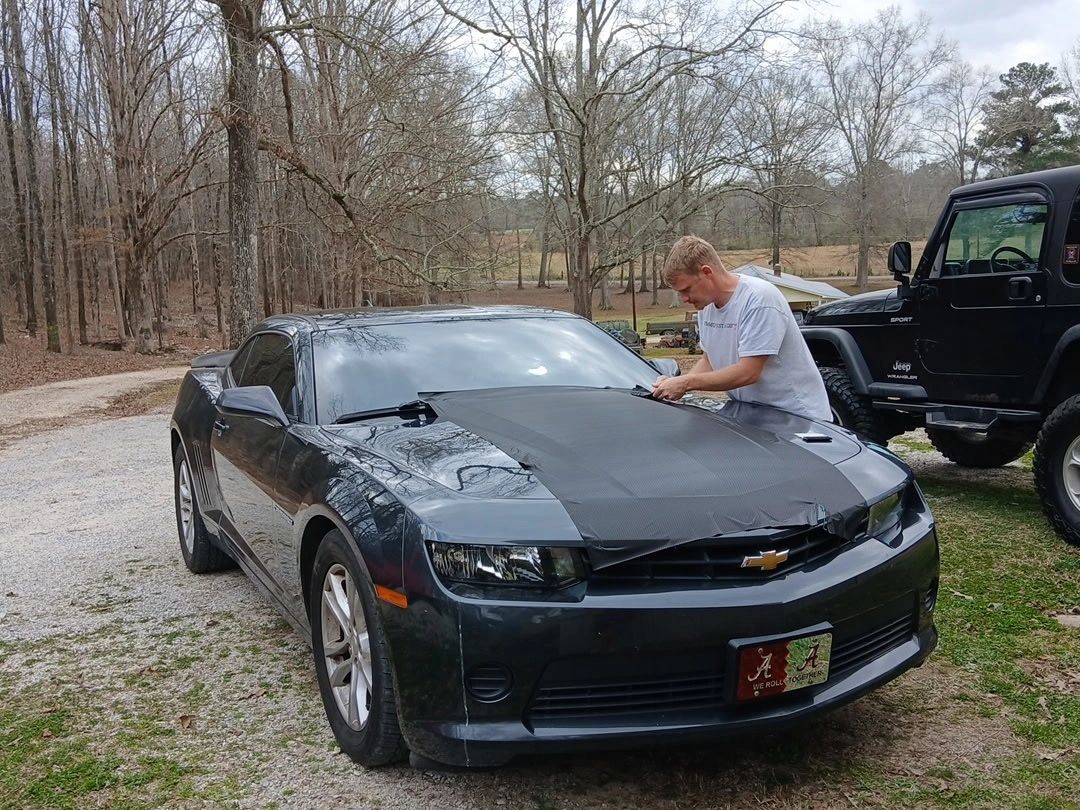 A man working on the hood of a black Chevrolet Camaro outdoors.